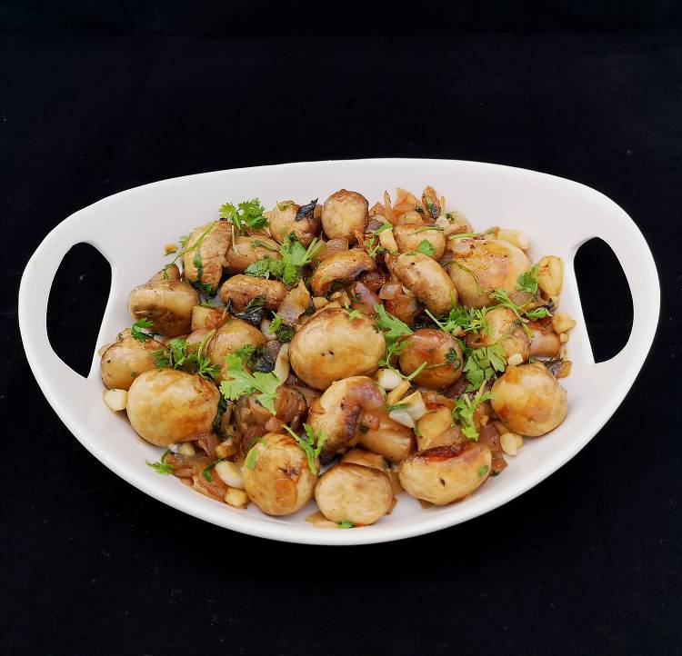close up view of garlic mushrooms garnished with finely chopped coriander leaves,  on a white platter