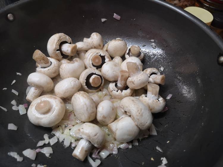 adding button mushroom to the kadai for preparing garlic mushroom