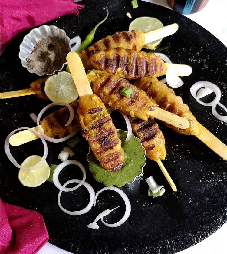 close up view of grilled kababs served with coriander chutney, onion and lime slices