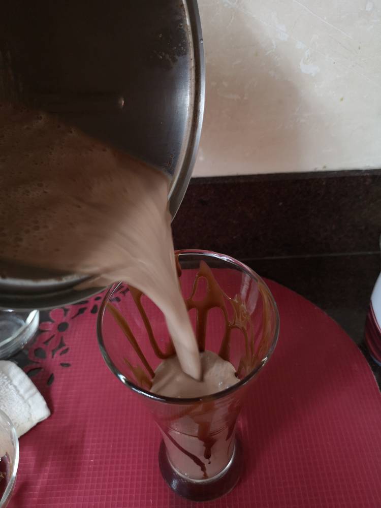 pouring thick and creamy chocolate milkshake into the glass with chocolate syrup