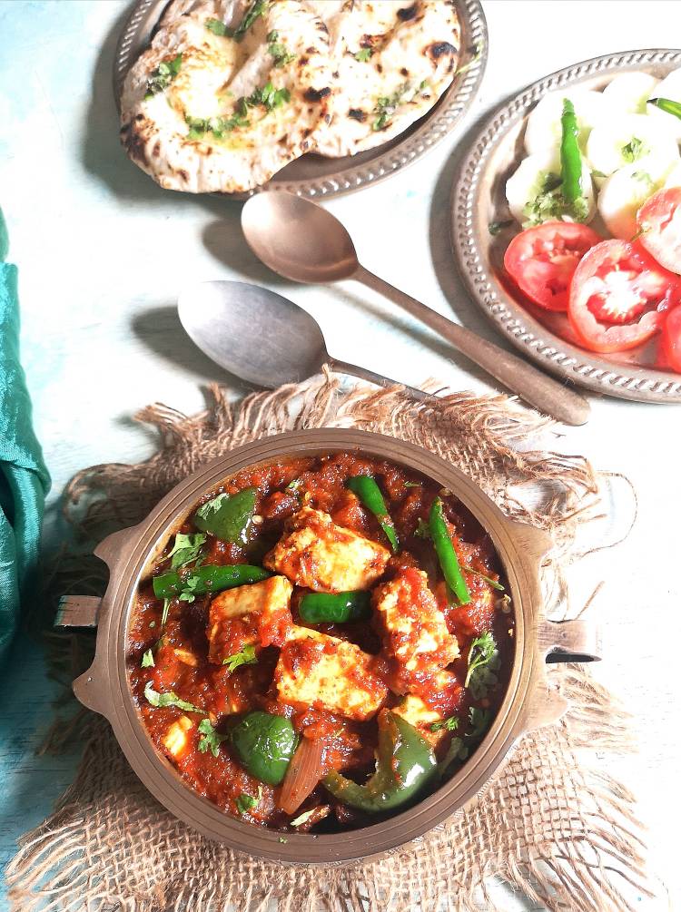 top view of delicious and flavoursome Kadhai Paneer served with garlic naan, cucumber , tomato salad along with green chilies.