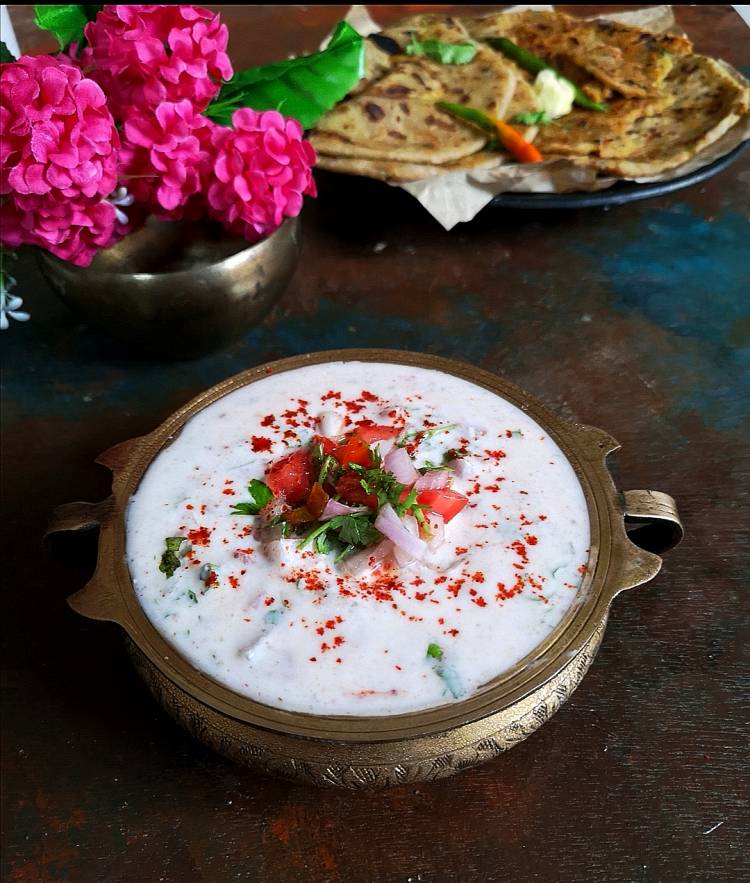 close up view of Onion Tomato Raita served in a brass bowl along with aloo parathas