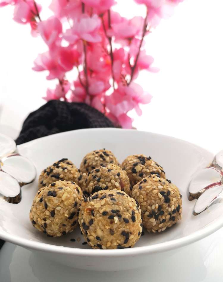how to make sesame energy bites, close up view of black and white sesame seeds energy bites served in a white bowl with pin flowers used as a decor