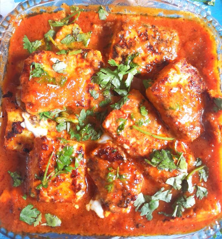 close up view of paneer cubes simmered in onion tomato gravy, garnished with finely chopped coriander leaves, ready to be served