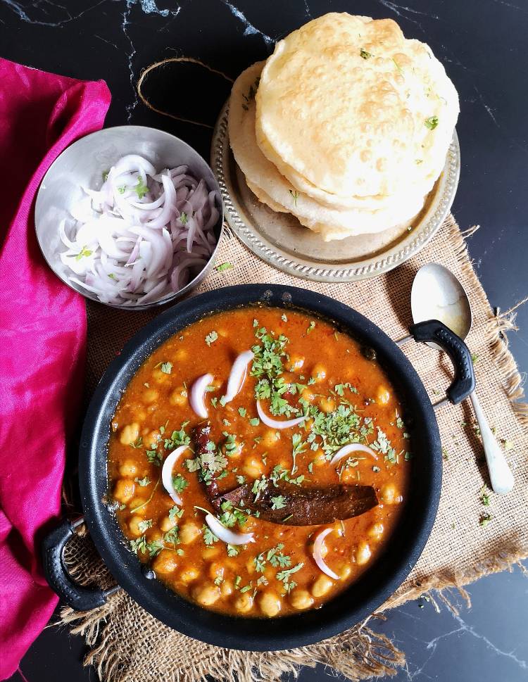 punjabi chole recipe, chole served with bhatura and sliced onions served on a black board and jute cloth