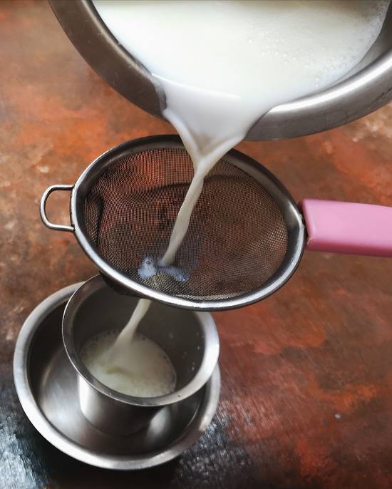 Pouring hot milk for filter kaapi in the dabarah in traditional south indian style 