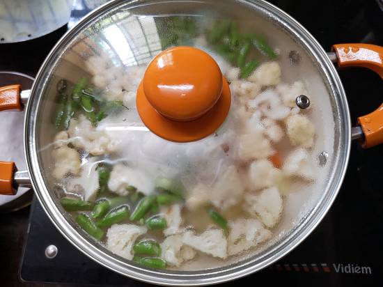 covering the cooking pan of boiling vegetables with a glass lid with orange handle