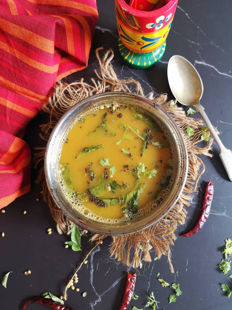 close up view of Mysore Rasam garnished with finely chopped coriander leaved and tadka of mustard seeds, curry leaves and hing