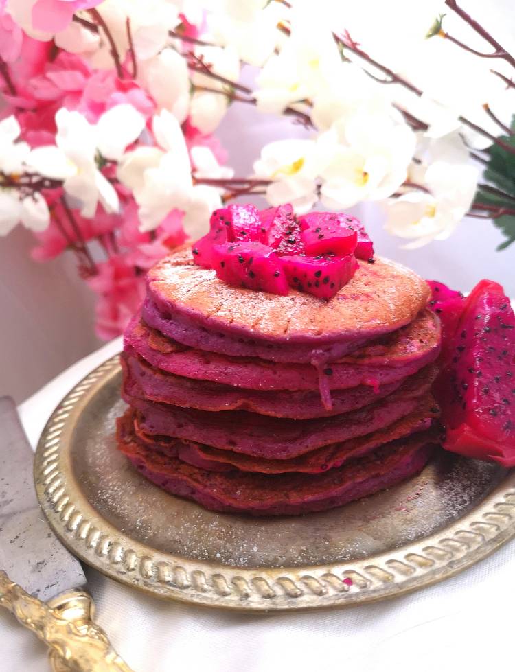stack of Pink Pitaya Pancakes topped with fresh small chunks of pink dragon fruit and decorated with pink and white flowers