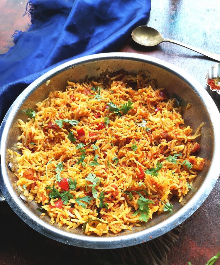tomato rice served in a steel pan, garnished with finely chopped coriander leaves and 
