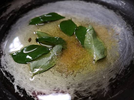 adding curry leaves and hing to hot ghee for tadka of tomato rasam