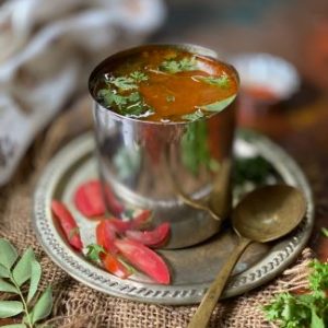 close up view of Tomato Rasam served in a steel tumbler, garnished with finely chopped coriander leaves , how to make Tomato Rasam without dal