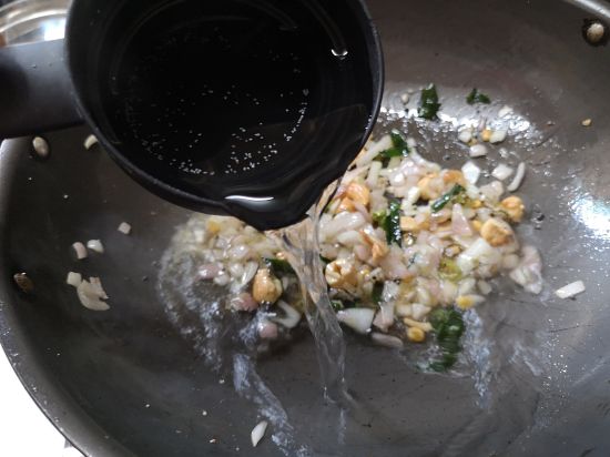 adding water to the pan with sauteed onions, cashew nuts and curry leaves, upma recipe
