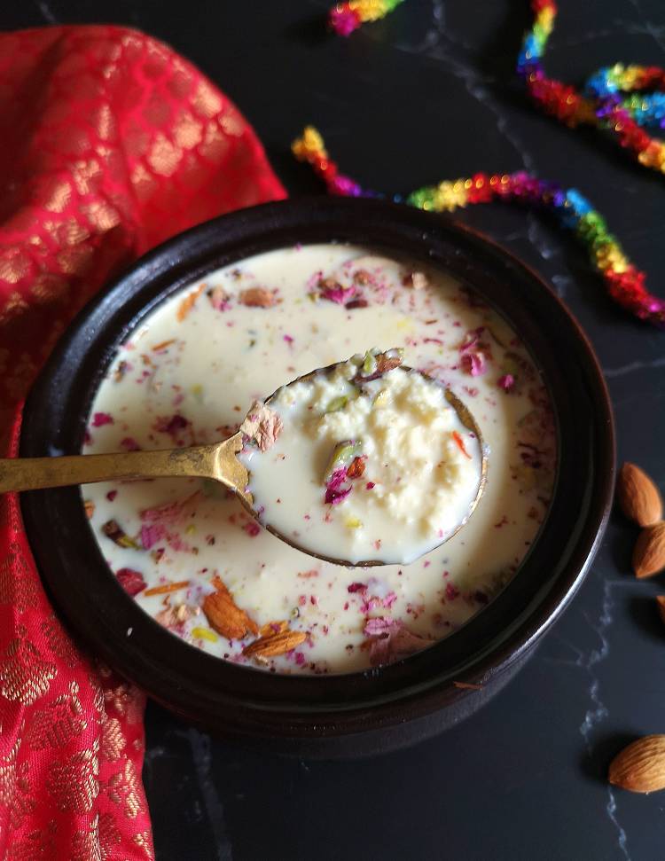 close up photo of a spoonful of delicious and creamy Kesar Paneer Kheer loaded with almonds, pistachios and dry rose petals, ready to be served