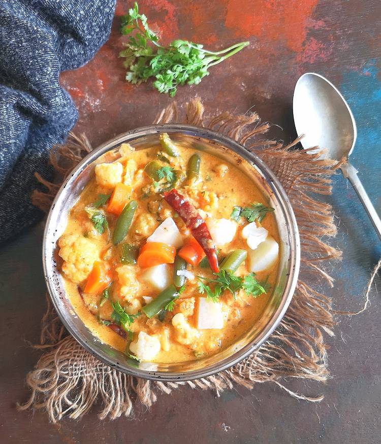 Overhead Photo of vegetable Korma served in a bowl on a jute clothe with a silver spoon and garnished with coriander leaves