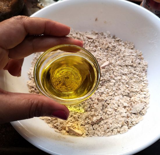 adding olive oil to oats and flour mixture with cinnamon and organic jaggery powder