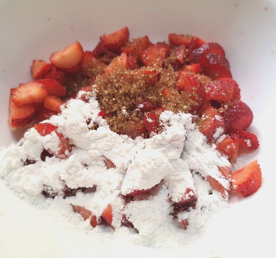 close up view of cut strawberries, mixed with powdered sugar and brown sugar