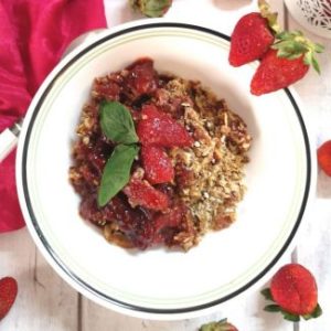 close up look of Strawberry Oats Crumble, garnished with cut strawberries, mint leaves, with a pink satin cloth,2 spoons and candle at the background, Recipe of Strawberry Oats Crumble, how to make strawberry oats crumble