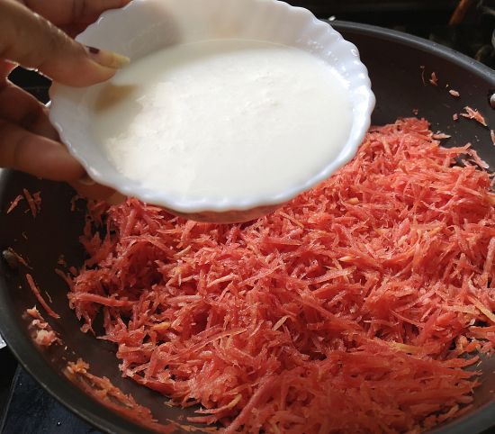 adding milk in grated carrots for gajar ka halwa