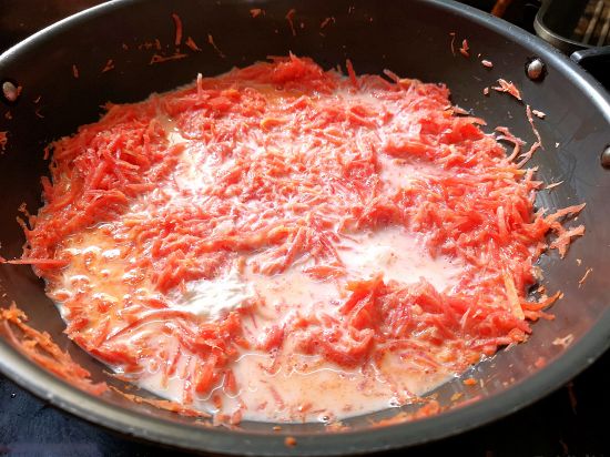 milk and grated carrots being cooked in a pan for gajar ka halwa