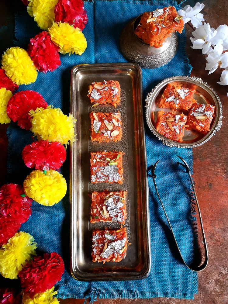 Recipe of Gajar Ki Barfi, How to make Carrot barfi, carrot barfi plated nicely on silver tray with flowers and blue jute cloth 