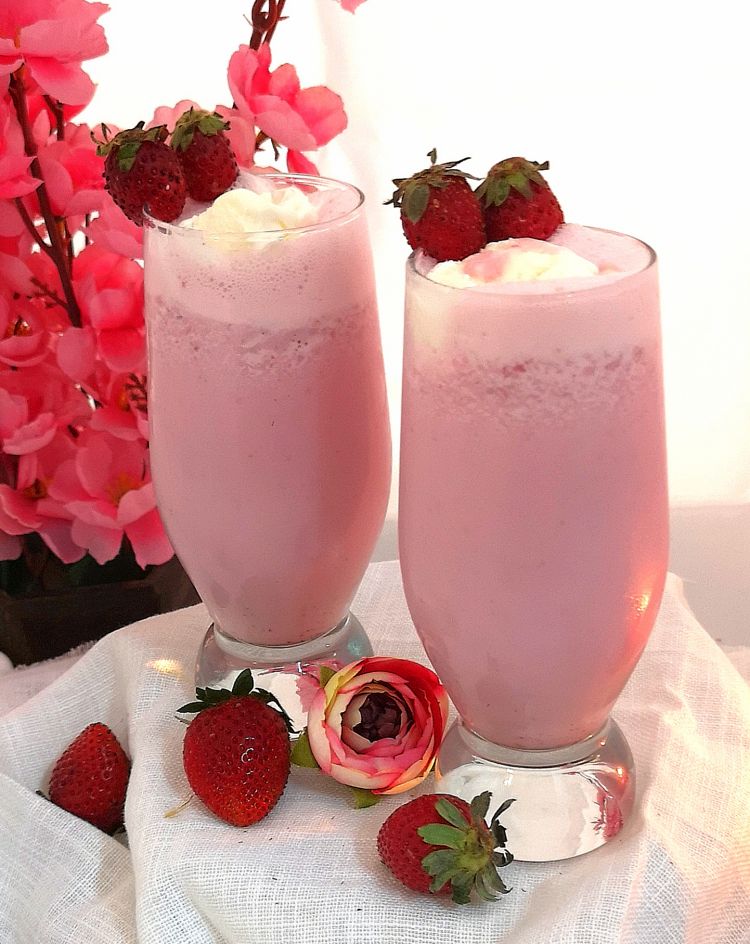 2 chilled glasses of strawberry milkshake garnished with fresh strawberries 