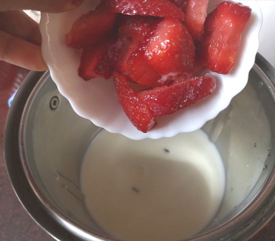 adding fresh cut strawberries to the blender for strawberry milkshake