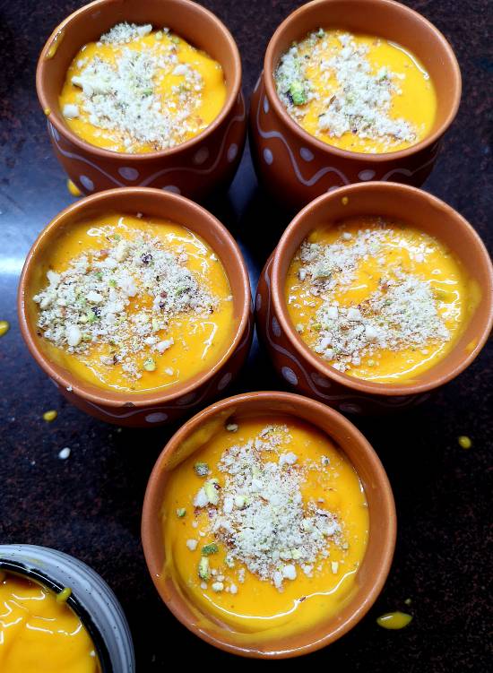 mango pulp poured in matkas and garnished with dry fruits powder, ready to be freezed