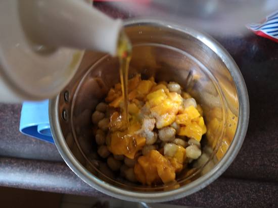 Adding extra virgin oilve oil into chickpeas and mangoes for mango hummus