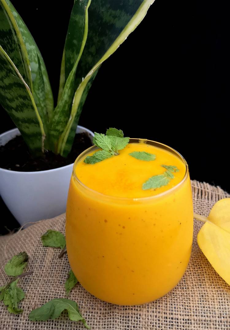close up photo of Mango Turmeric Smoothie garnished with fresh mint leaves and a snake plant in the background